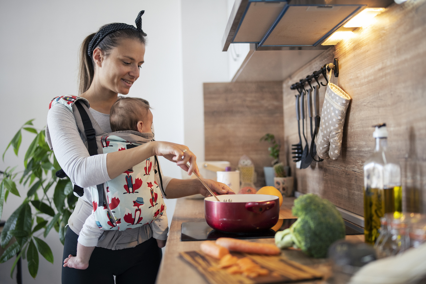 Multi-task mother cooking and taking care of newborn son.