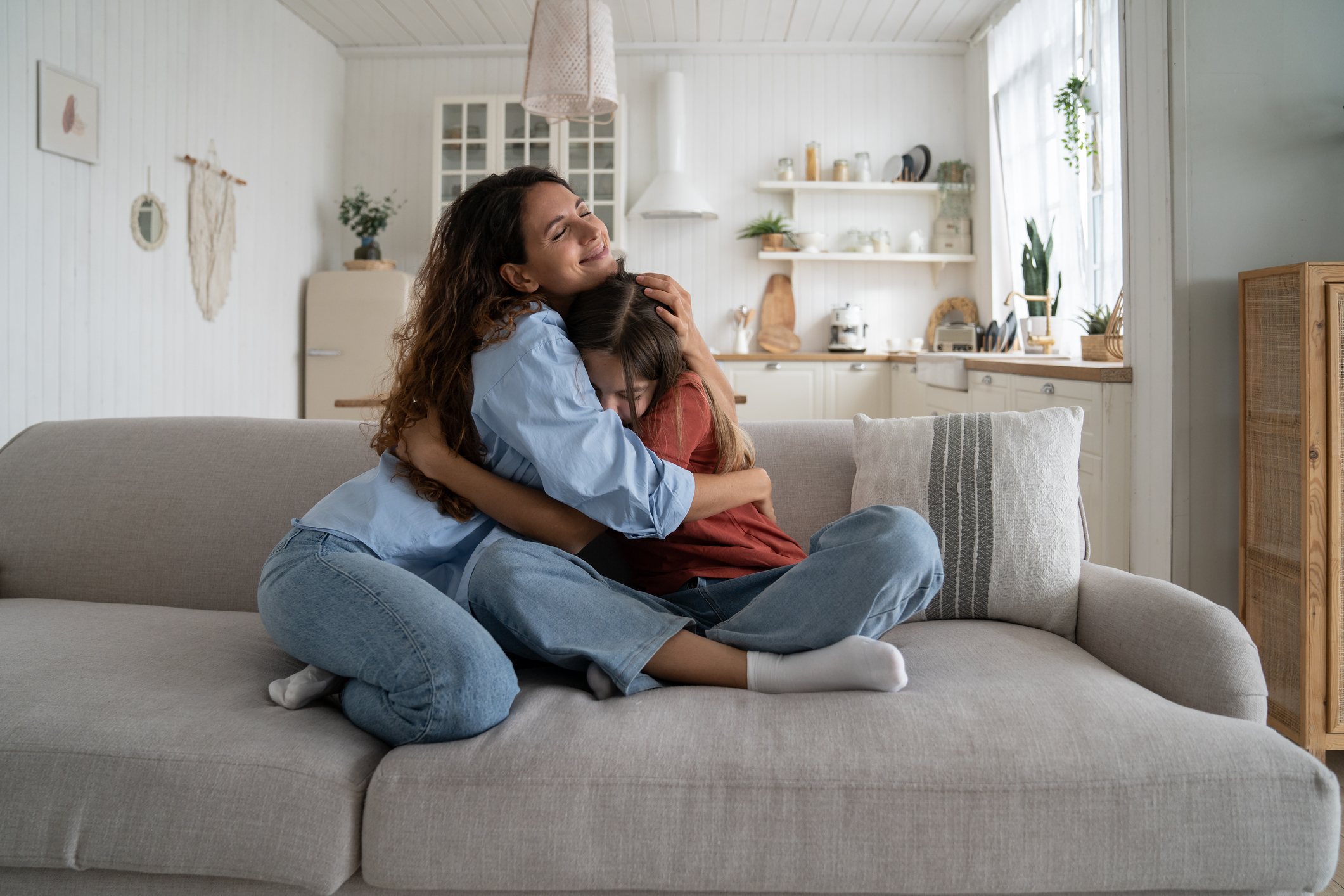Friendly loving mother and daughter hugging sits on sofa in spacious living room of own home