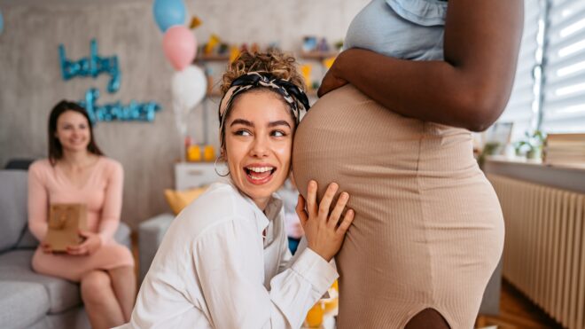 Baby shower guest puts her ear up to pregnant mom's belly